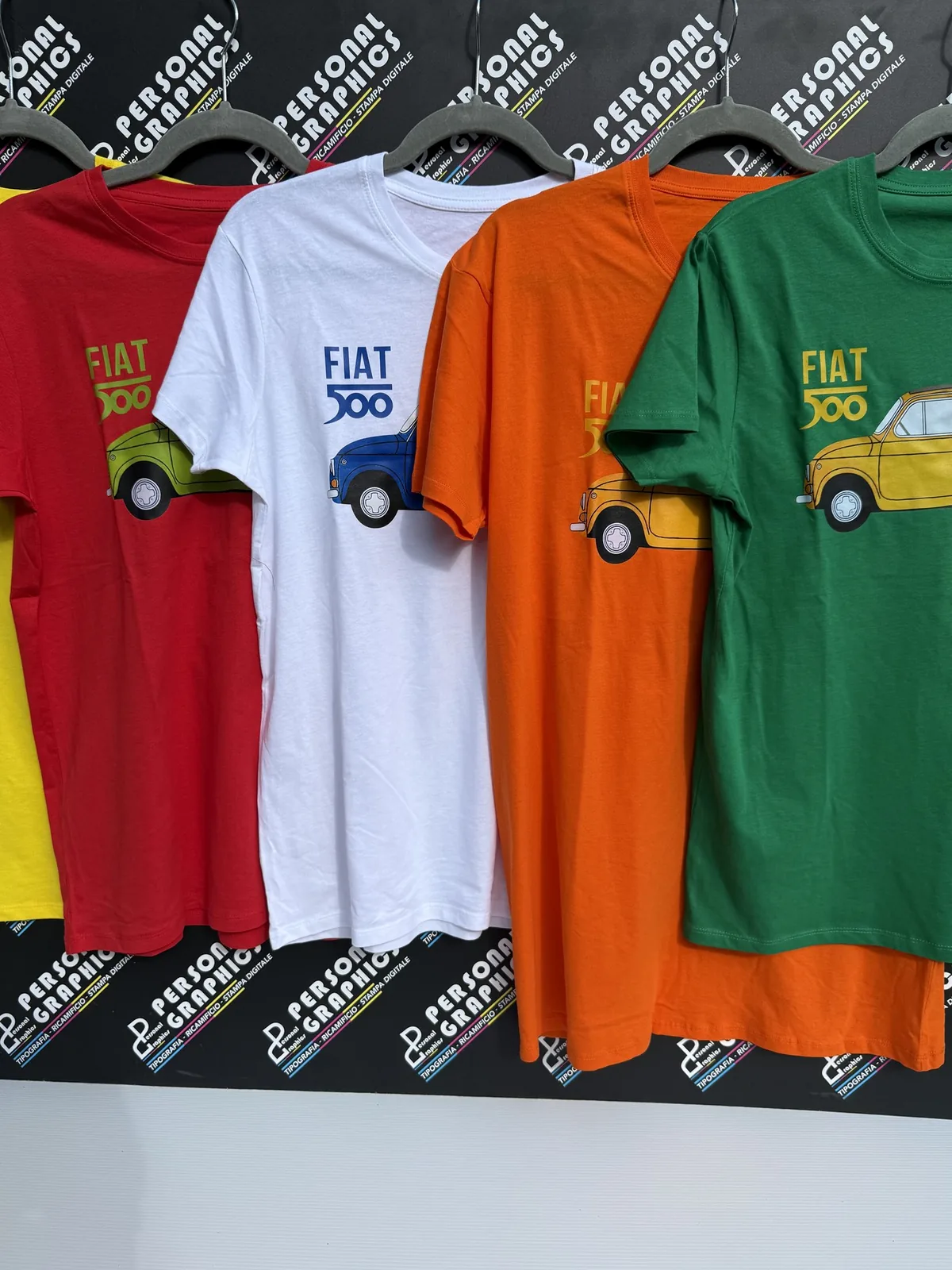 T-shirt Fiat 500 di quattro colori appese in negozio