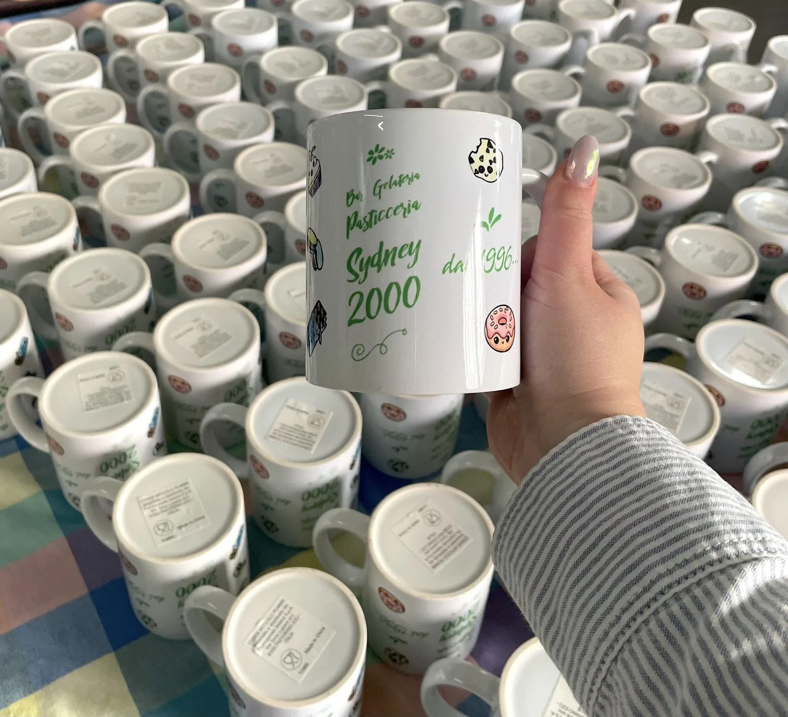 Tazze bianche personalizzate con grafica verde e dorata, una in mano fra le altre