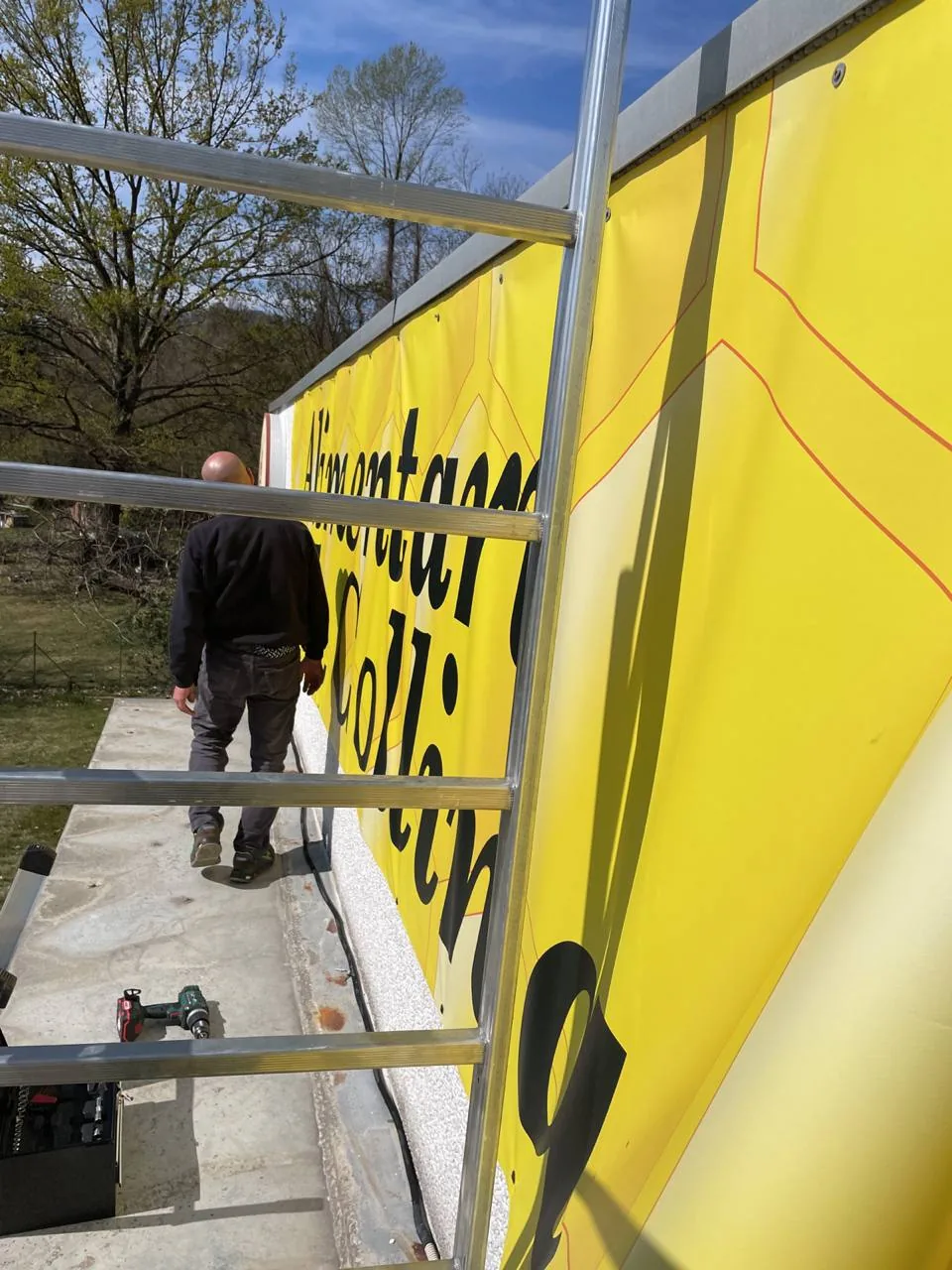Posa di un grande banner giallo su una facciata, con il posatore sul trabattello
