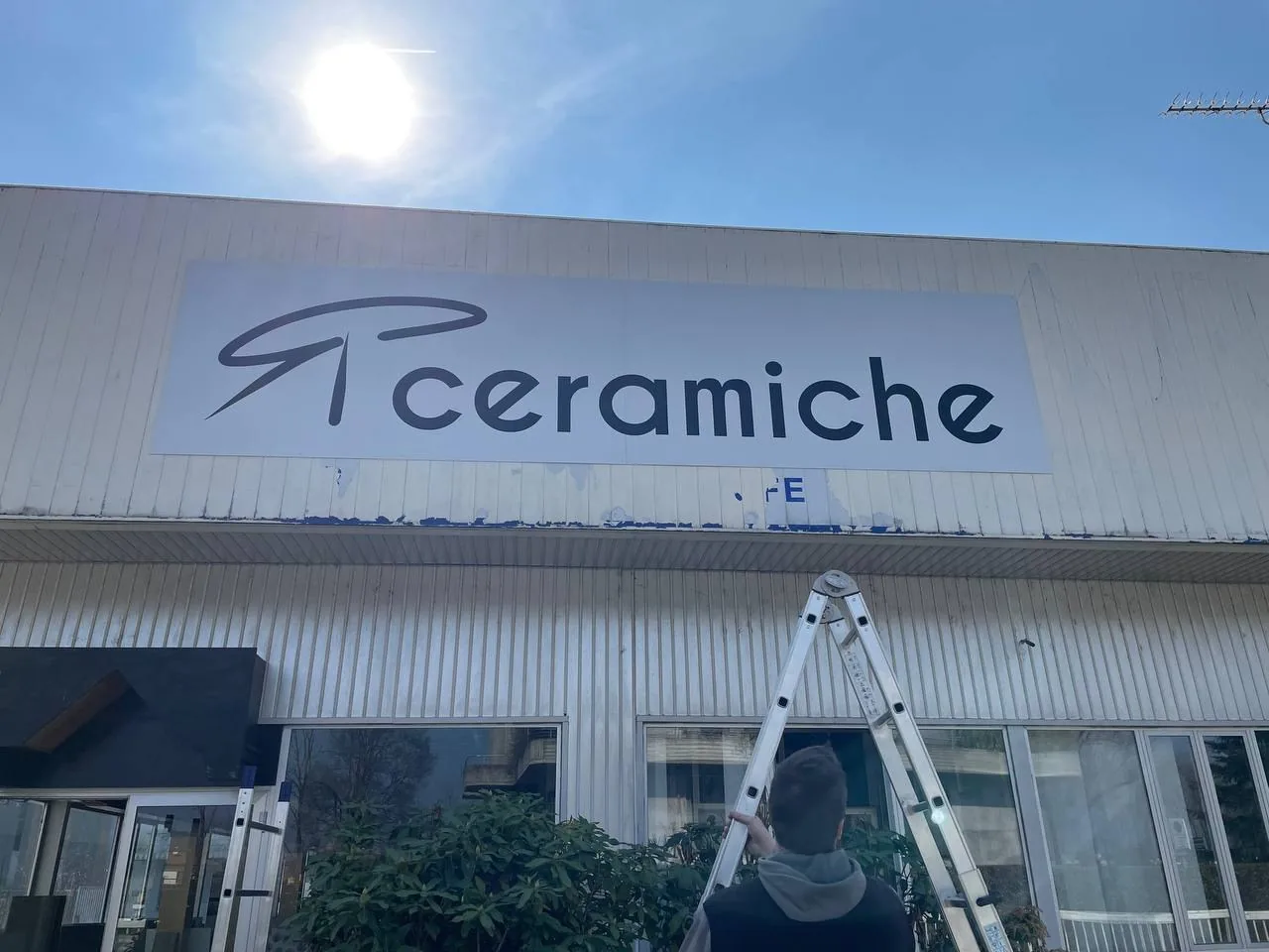 Insegna R Ceramiche sulla facciata del capannone, durante la posa