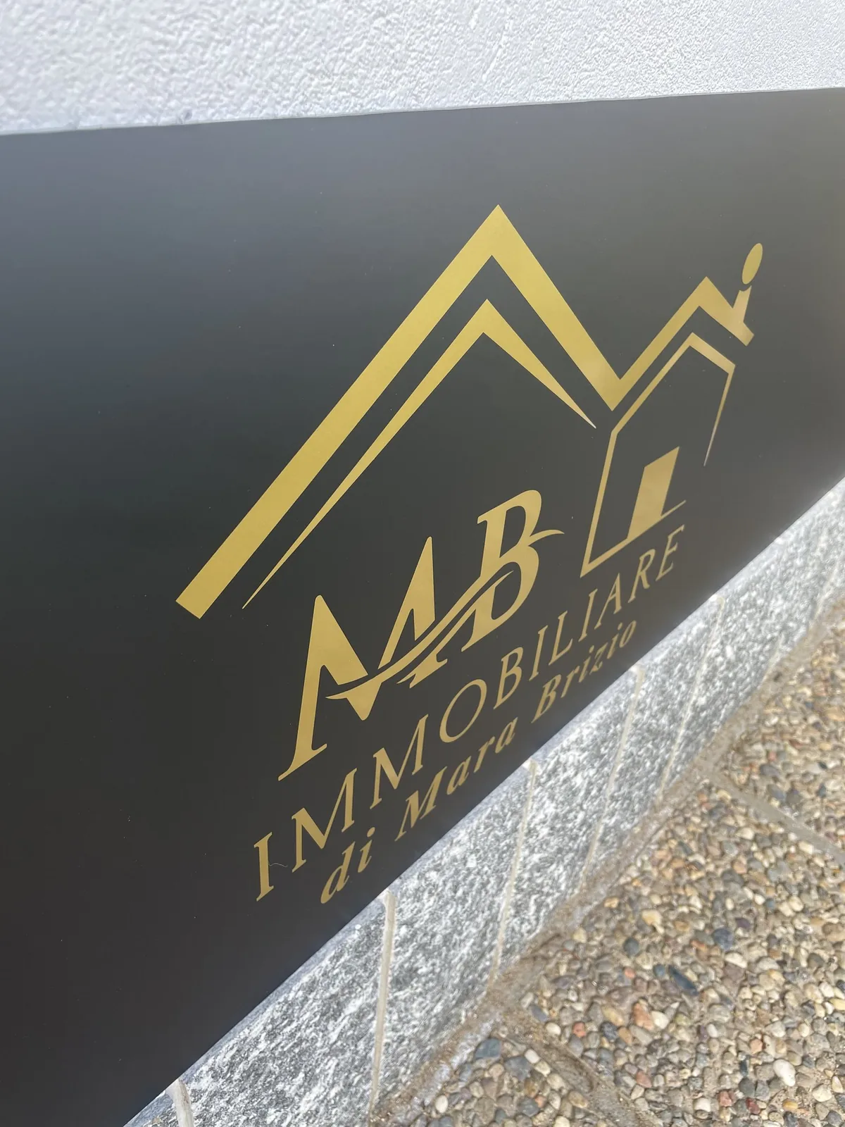 Dettaglio del logo oro in rilievo sull’insegna MB Immobiliare