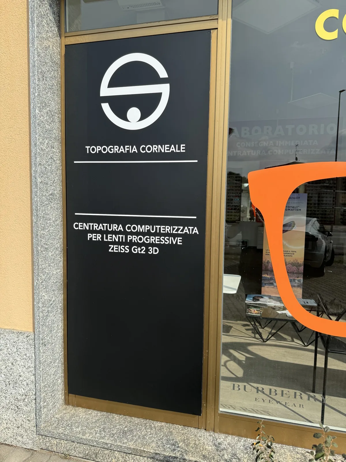 Vetrina di un’ottica con il pannello nero Topografia corneale e l’occhiale arancione