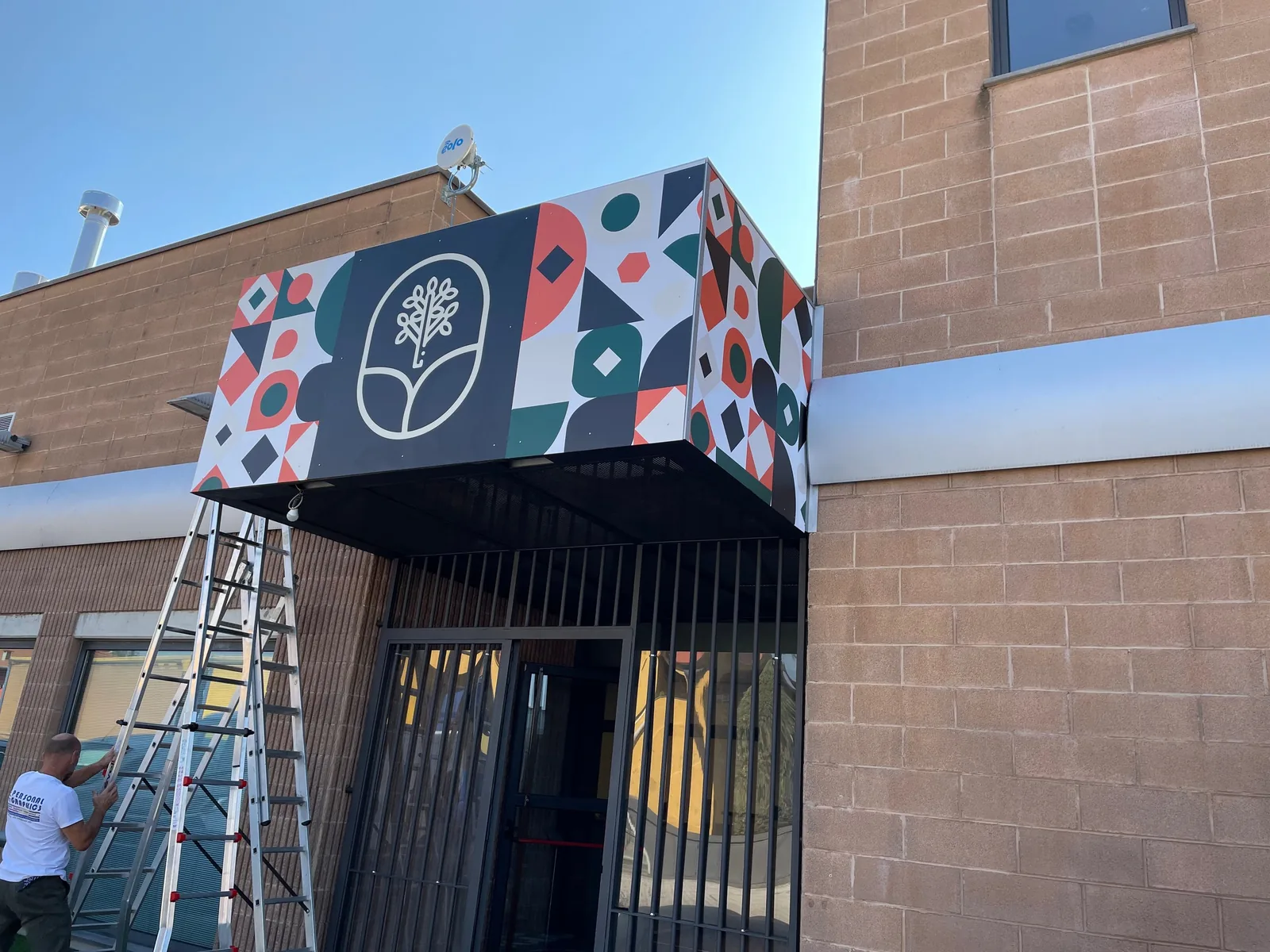 Pensilina con la grafica geometrica Comero sopra l’ingresso, durante la posa