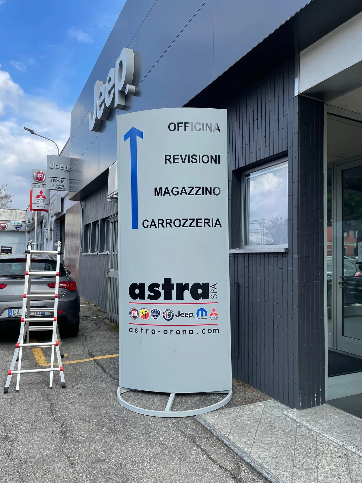 Totem Astra con le indicazioni officina, revisioni, magazzino e carrozzeria davanti alla concessionaria