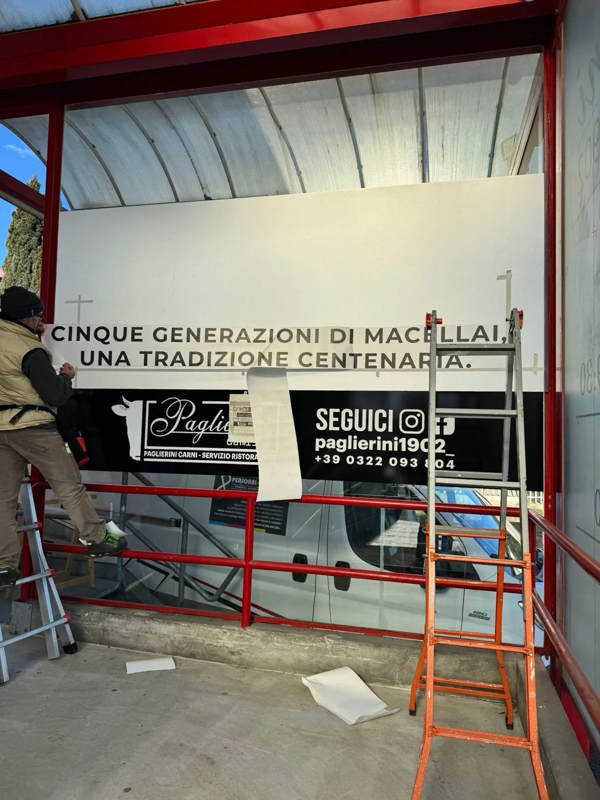 Posatore che applica il logo Paglierini sulla vetrata, con la scritta «Cinque generazioni di macellai» già prespaziata