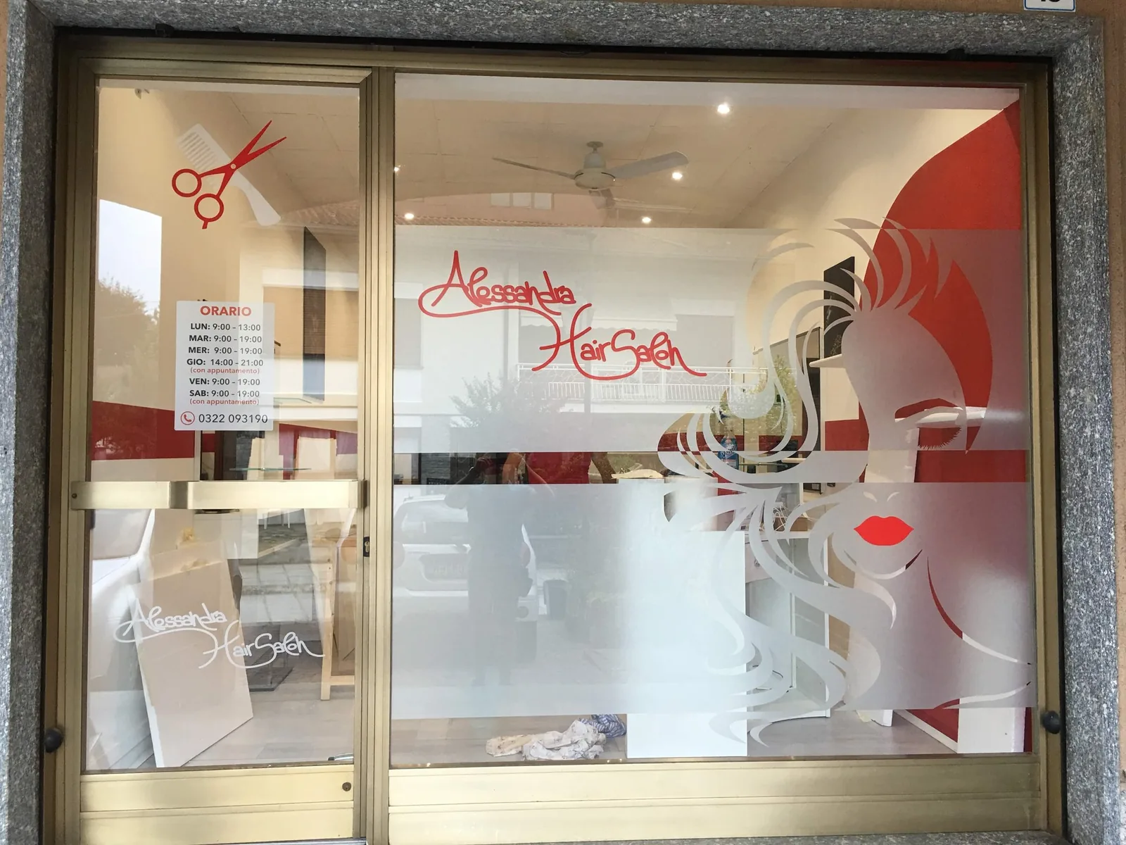 Vetrina del salone Alessandra Hair Salon con volto stilizzato, forbici rosse e fasce satinate