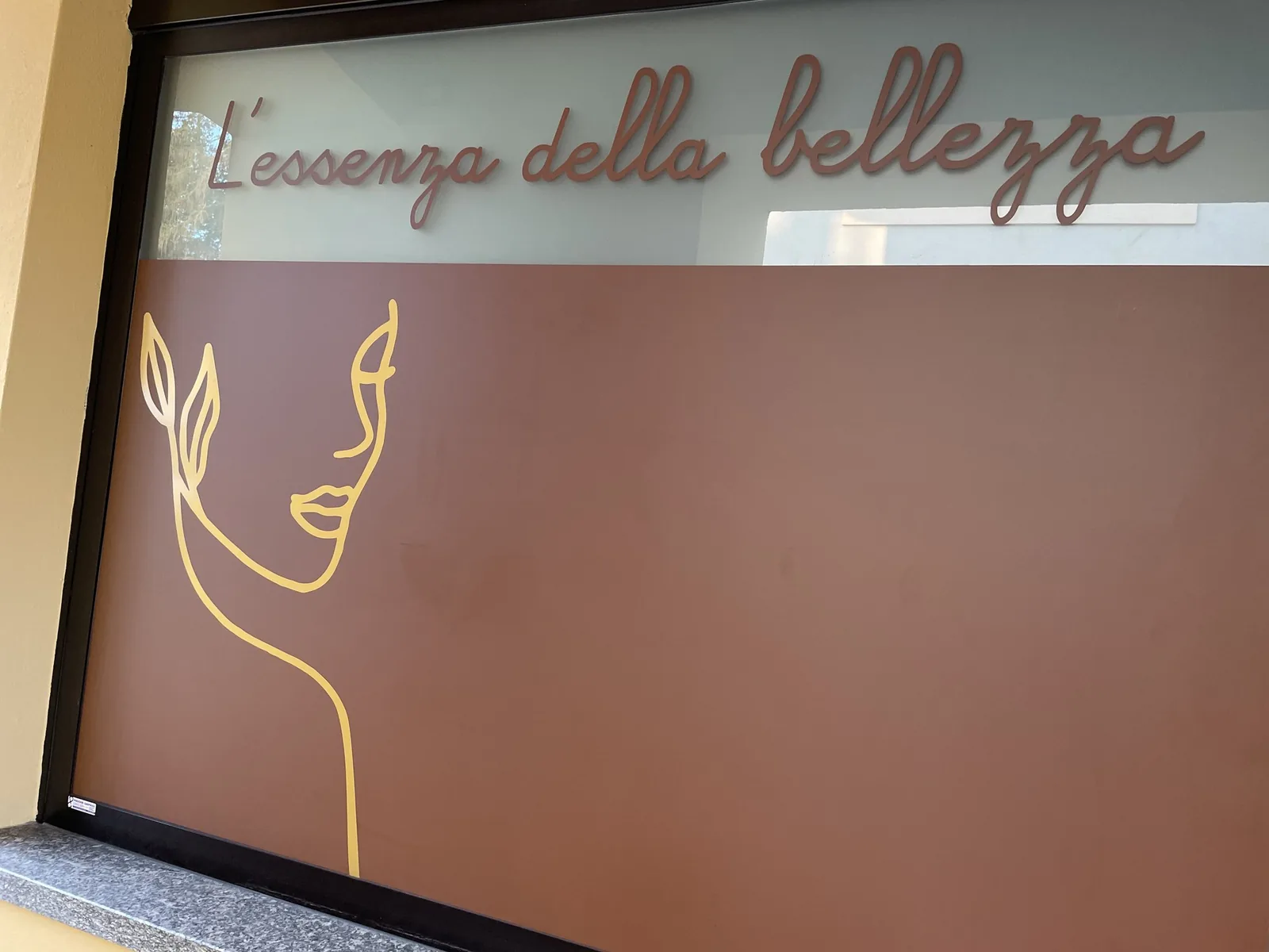 Vetrina con scritta «L’essenza della bellezza» e volto stilizzato in pellicola sagomata